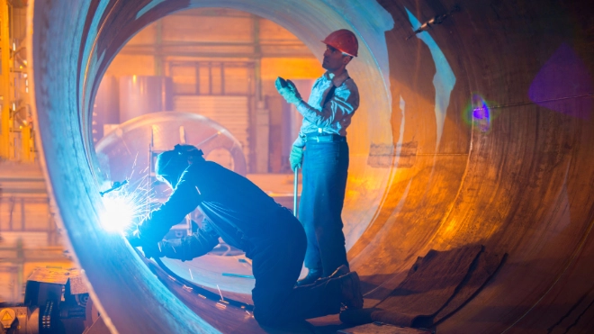 Two male welders working on metal pipe