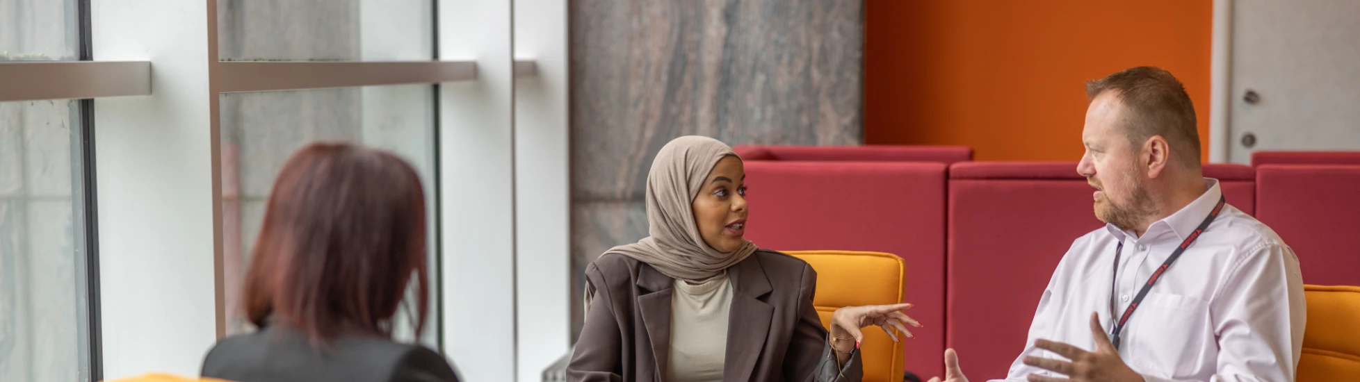 Two women and man on orange seats meeting