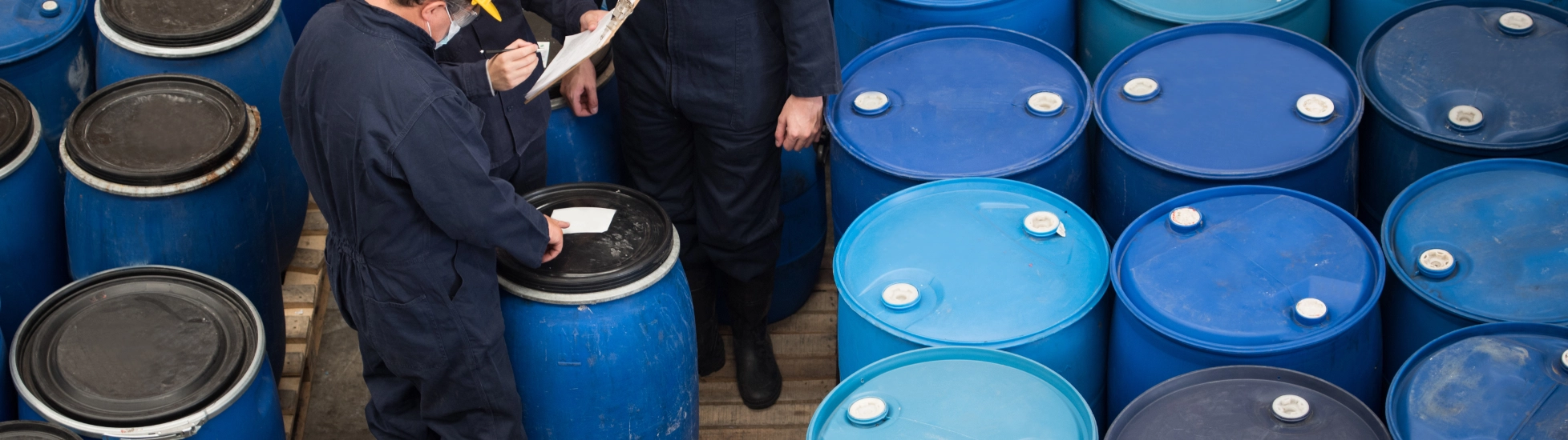 Three men inspecting chemical drums