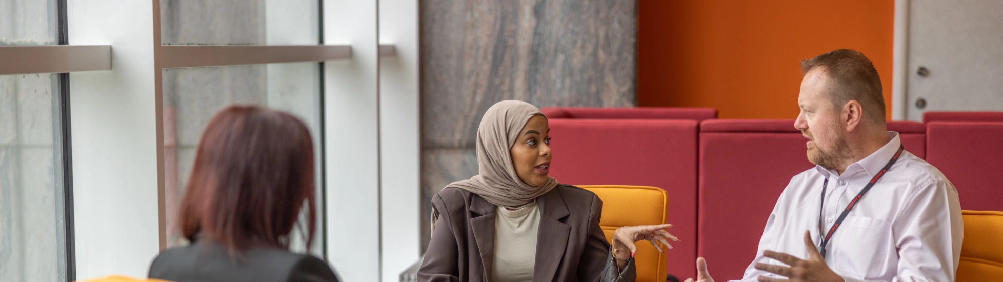 Two women and man on orange seats meeting